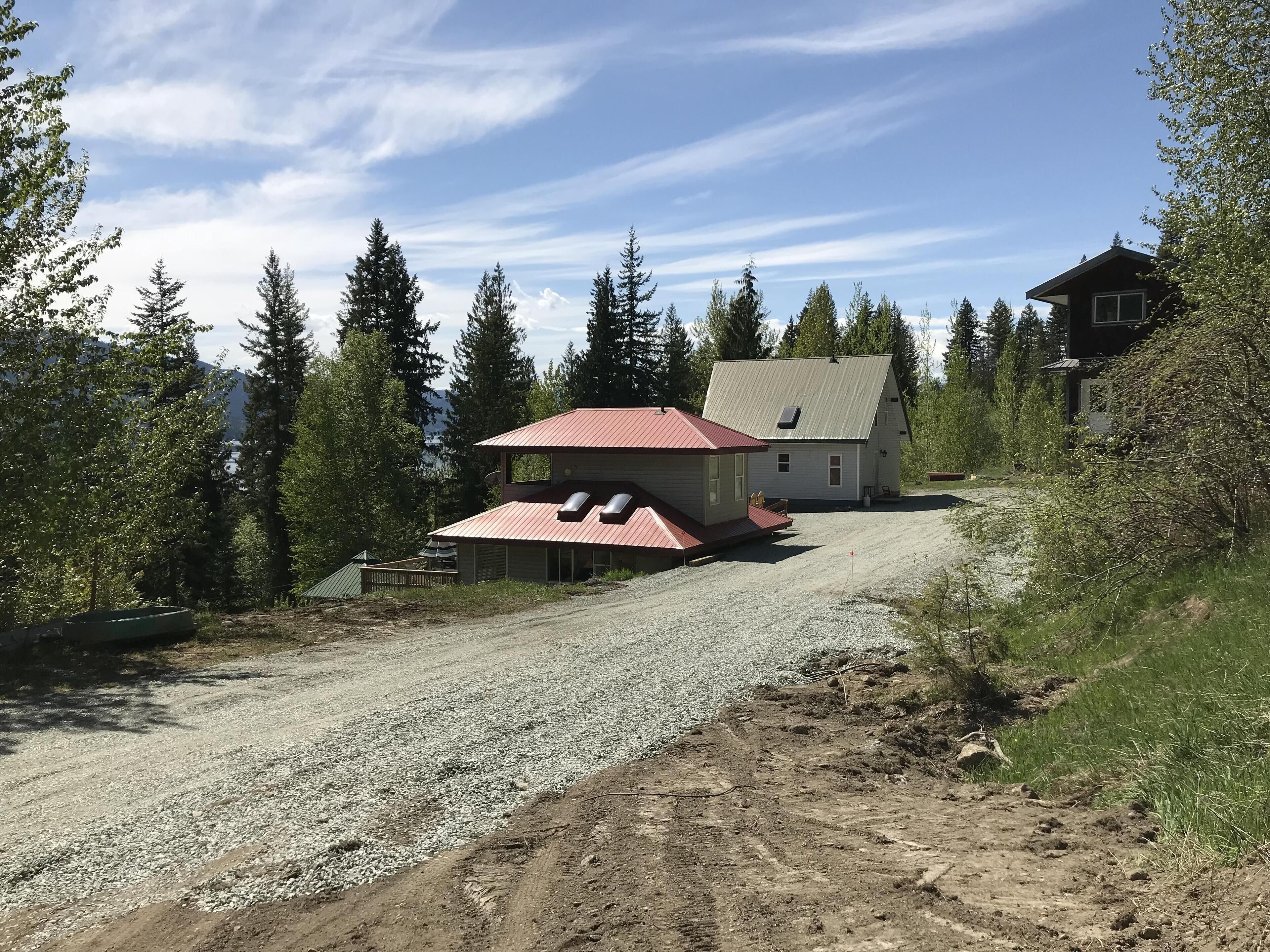 Une maison avec un toit rouge, une allée en gravier et un paysage boisé en arrière-plan.