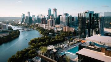 A modern cityscape with high-rise buildings, a river, and a rooftop pool area.
