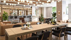 Un intérieur moderne avec une longue table à manger en bois, des chaises noires et un coin cuisine à l’arrière-plan.