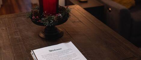 Une table en bois sur laquelle est posée une bougie rouge dans un joli photophore, un panneau d’accueil et une lampe en arrière-plan.