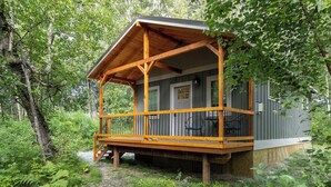A cabin with a wooden porch, a door, and a window. - Forestlane Cottage 2 (Palmer)