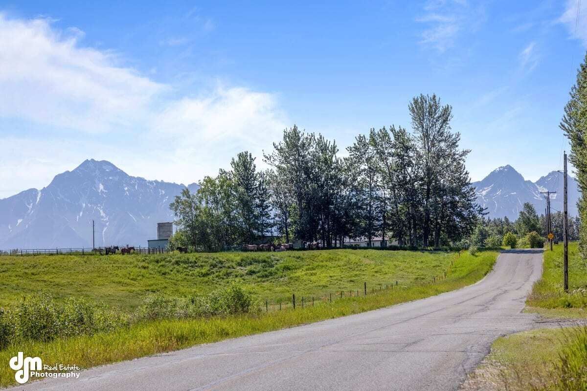 A rural road with a mountain backdrop, a fenced pasture, and a small building.