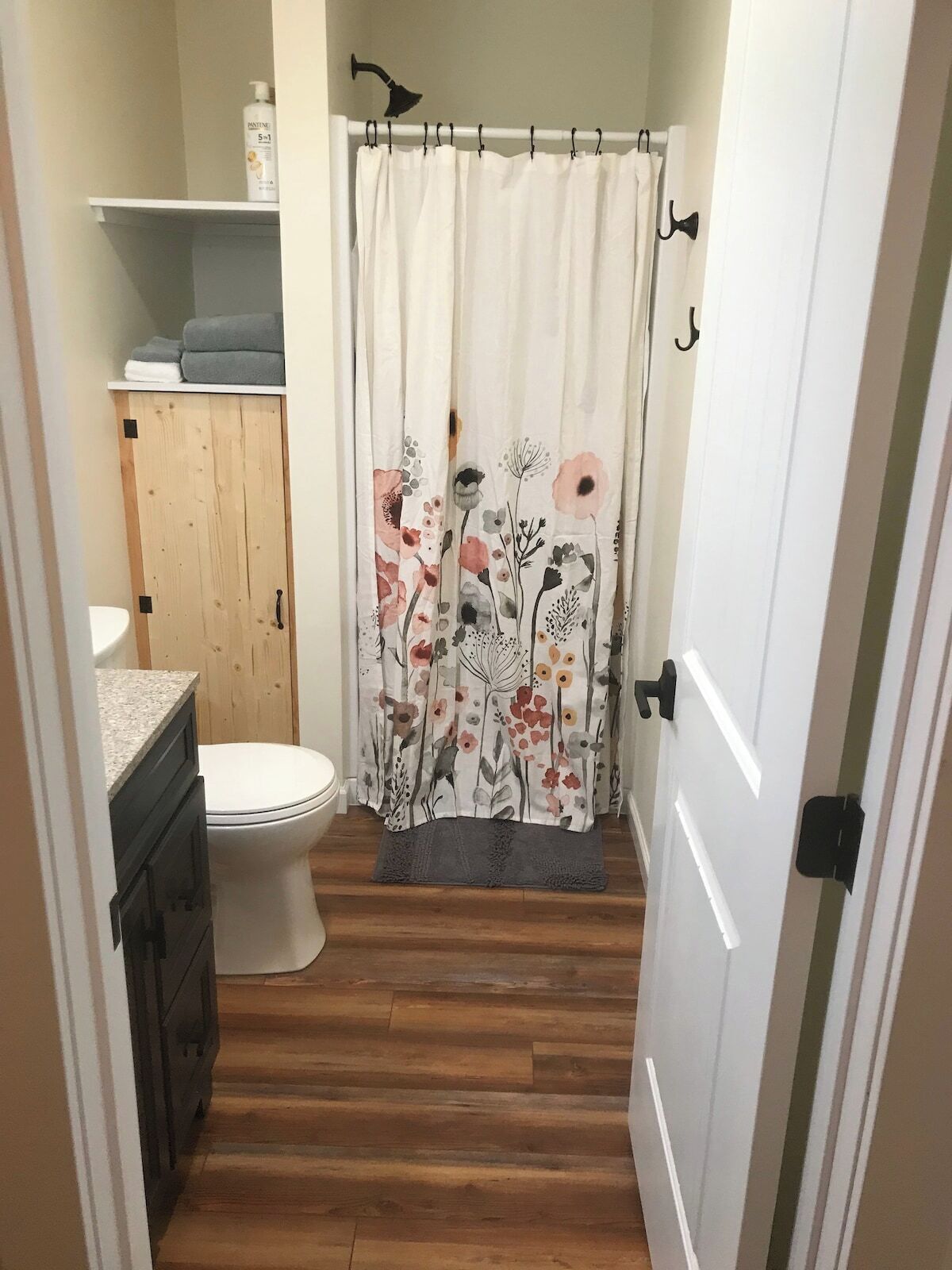 Un baño estrecho con inodoro, mueble de madera y cortina de ducha estampada con motivos florales.