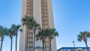 Un hotel alto con varios balcones, palmeras en la entrada y un cartel que dice "Grande Surf Club 8601".
