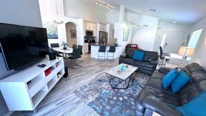 Un salon moderne doté d’un téléviseur à écran plat, d’un canapé, d’une table basse et d’un coin repas avec des chaises.