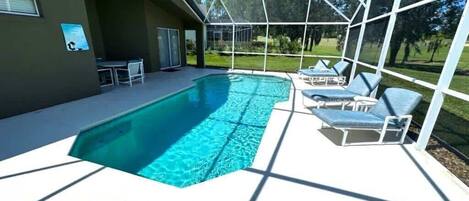 A covered swimming pool with lounge chairs and a patio area.