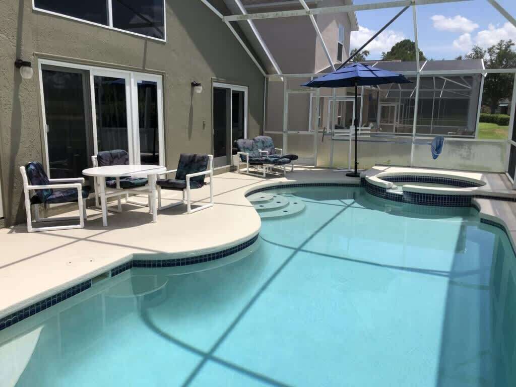 A swimming pool with a sunken hot tub, surrounded by a covered patio with chairs and a table.