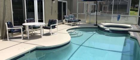 A swimming pool with a sunken hot tub, surrounded by a covered patio with chairs and a table.
