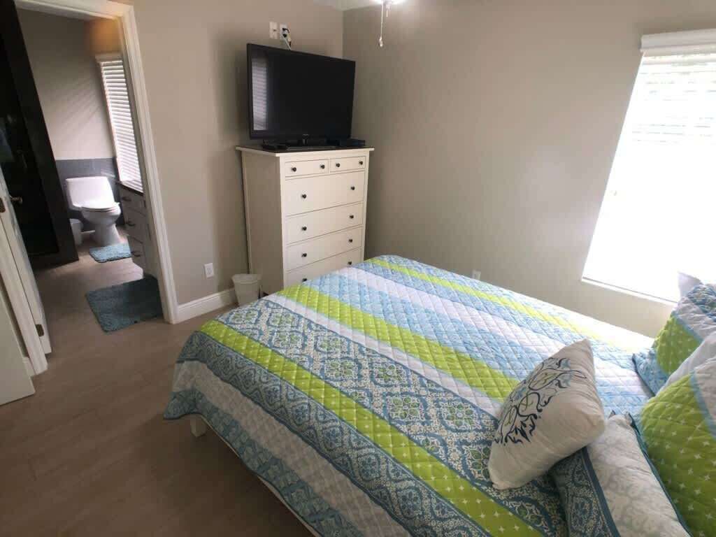 Ein Schlafzimmer mit einem Bett, einer Kommode, einem Fernseher auf der Kommode und einem Fenster mit Jalousien.
