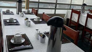 Ein Essbereich mit gedeckten Tischen für das Frühstück, darunter Kaffeekannen und Teekannen, und Blick durch große Fenster.