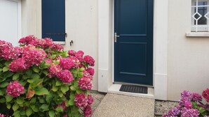 A house with a blue door, a window with a diamond pattern, and pink flowers in the foreground. - Pretty little house 100m from the beach and shops, with WIFI connection (Bretignolles-sur-Mer)