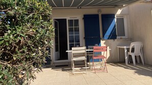 A patio with a table and chairs, a blue door, and a window with a view of the sky. - Pretty little house 100m from the beach and shops, with WIFI connection (Bretignolles-sur-Mer)