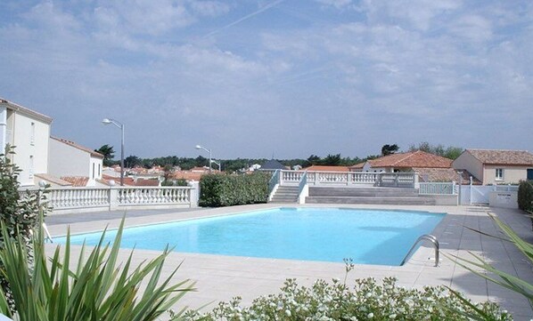 A swimming pool with a white fence, surrounded by greenery and residential buildings.