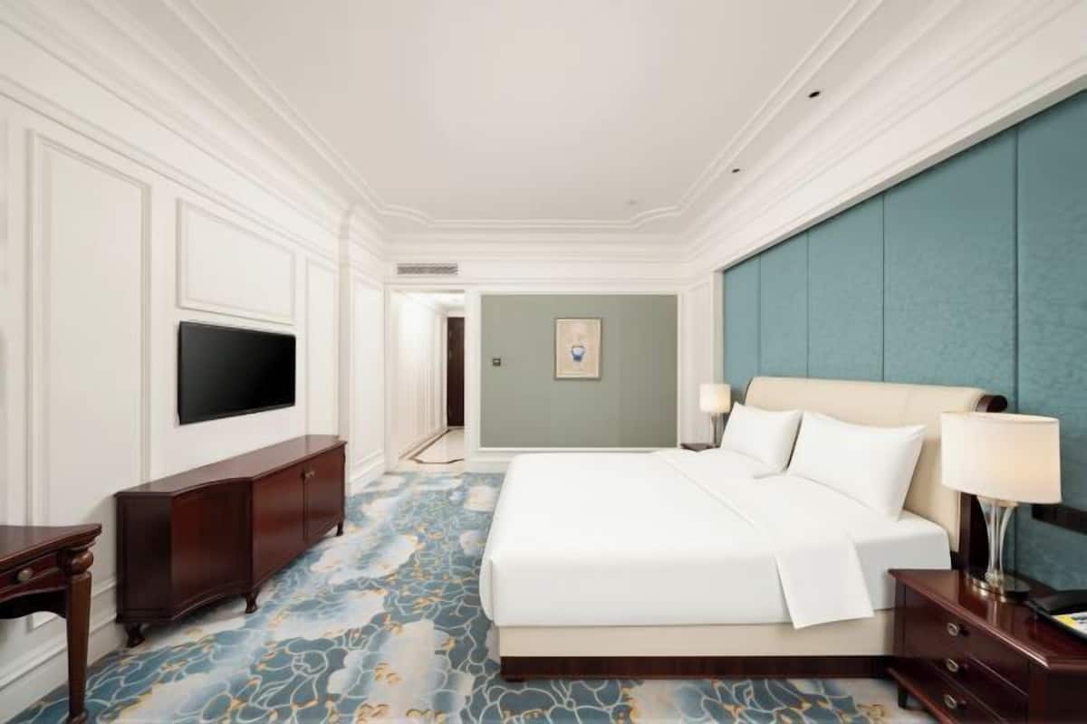 A hotel room with a large bed, a TV, a desk, and a blue accent wall.