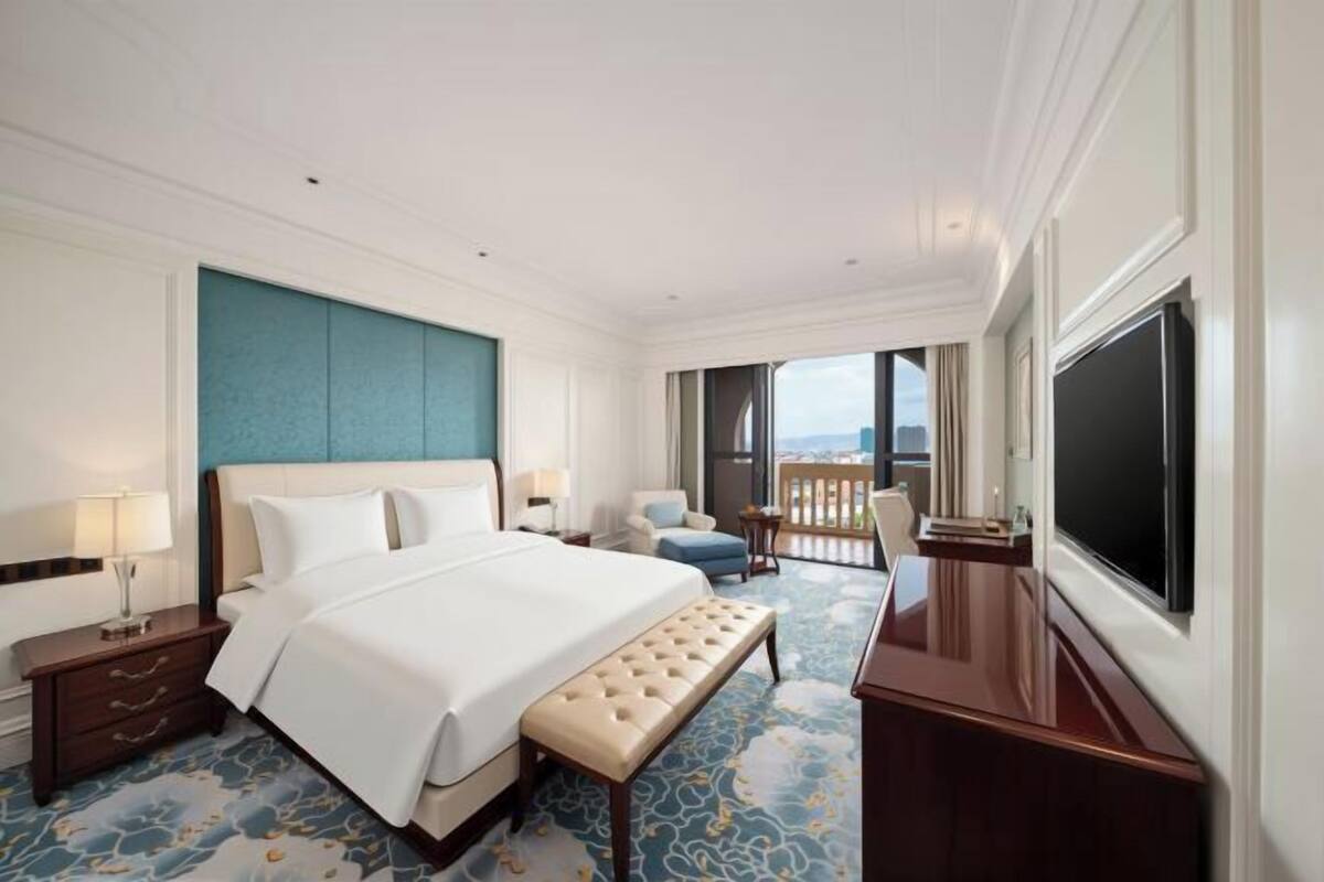A hotel room with a large bed, a bench, a desk, a chair, and a TV.
