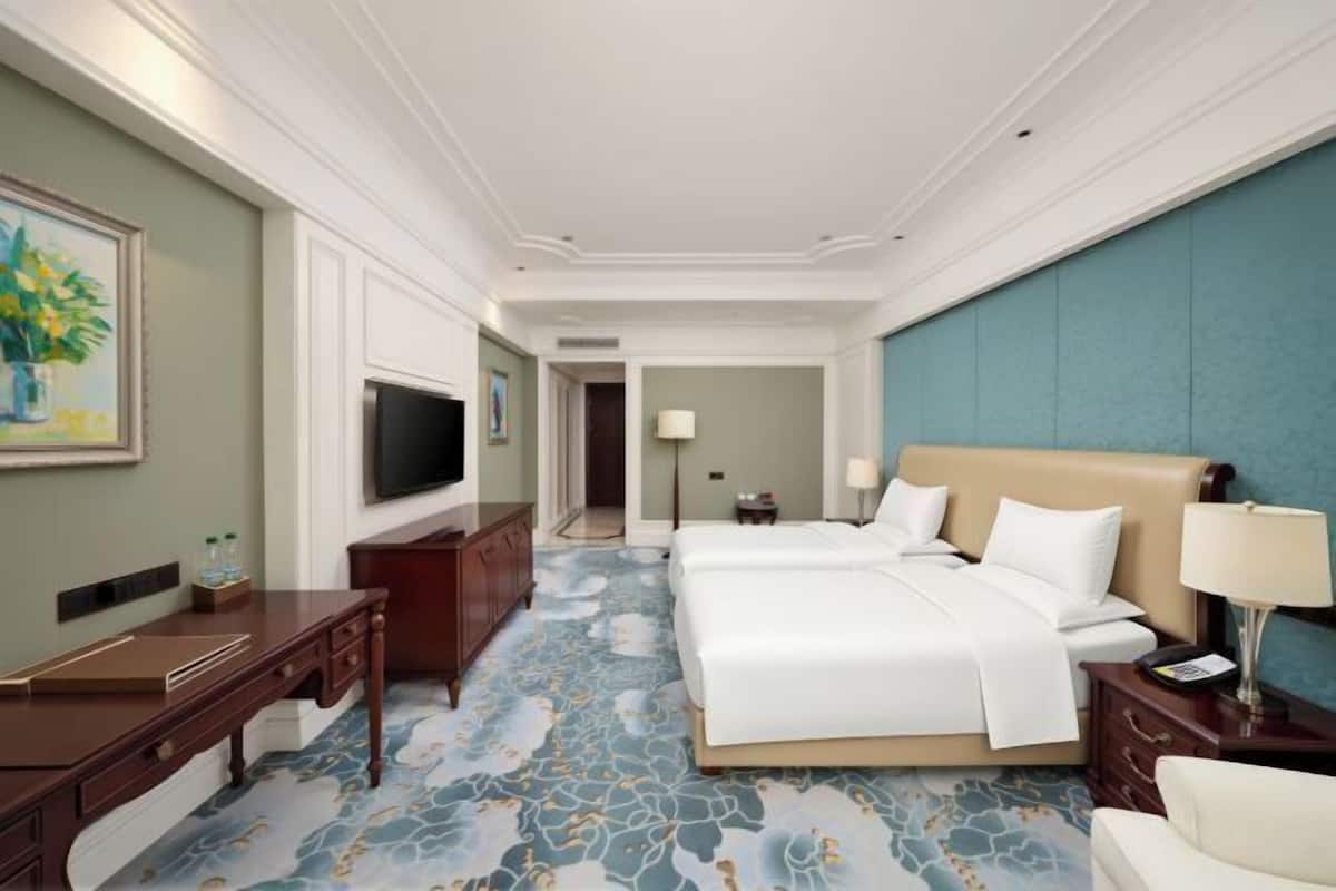 A hotel room with a large bed, a desk, a television, and a bathroom in the background.