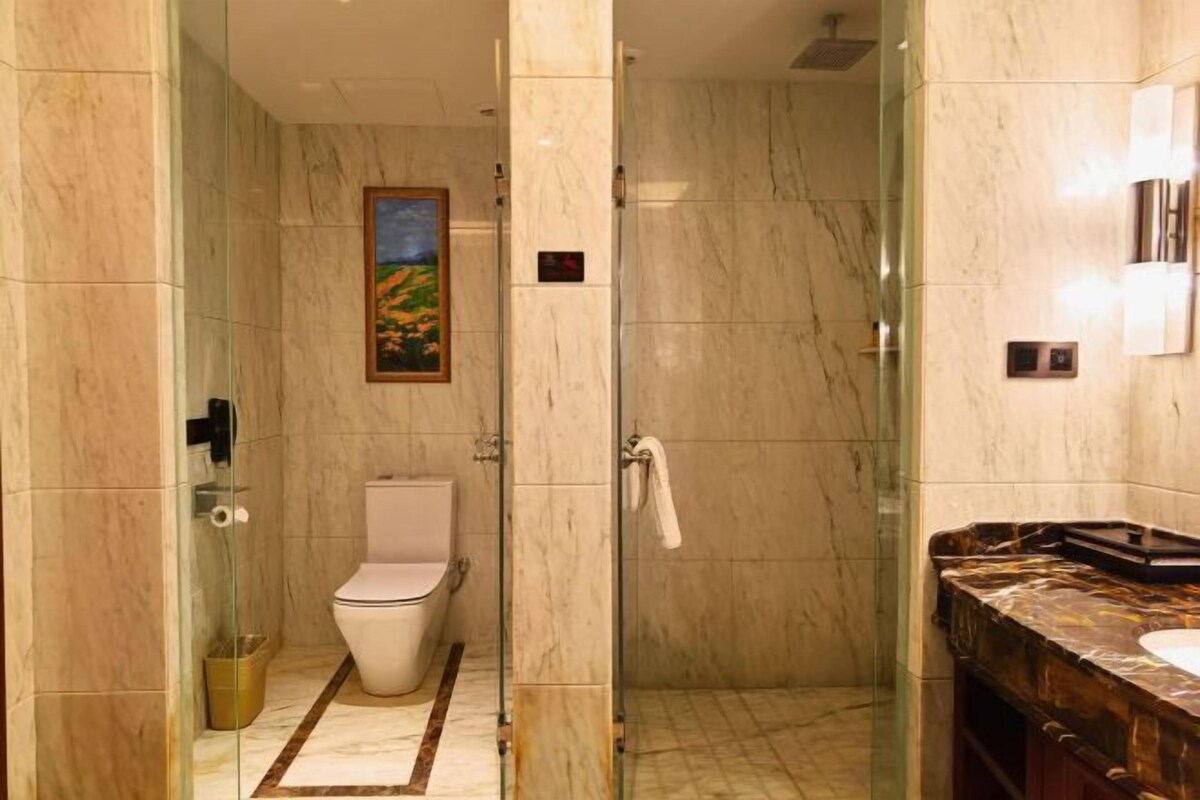 A modern bathroom with a glass-enclosed shower, a marble floor, and a marble vanity with a sink.