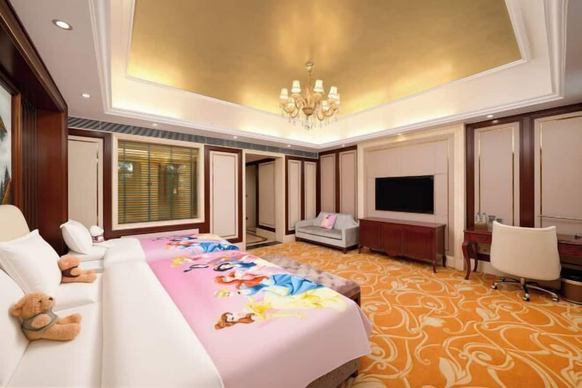 A hotel room with a large bed, a television, a desk, and a chair.