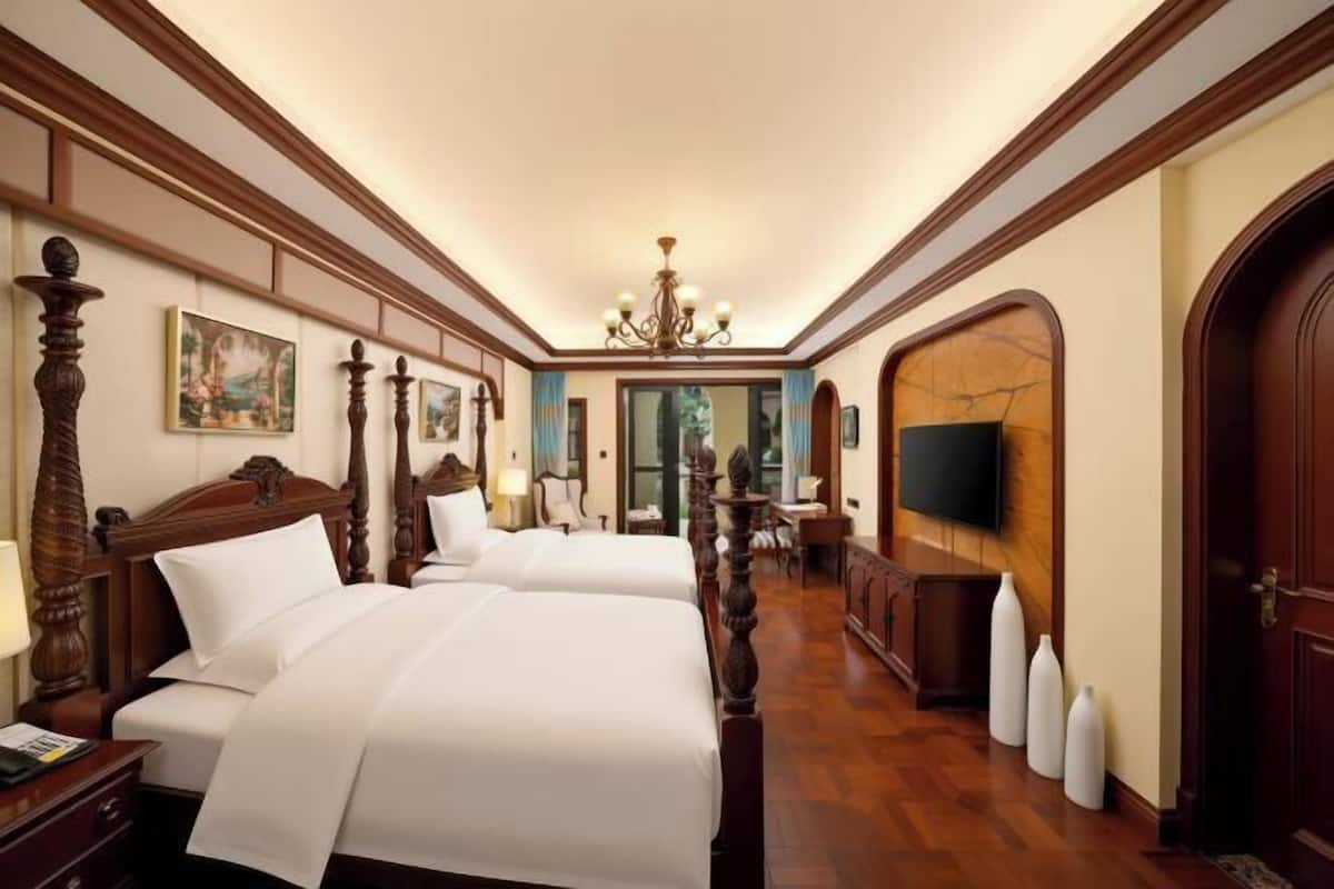 A hotel room with two beds, a chandelier, a television, and a wooden floor.