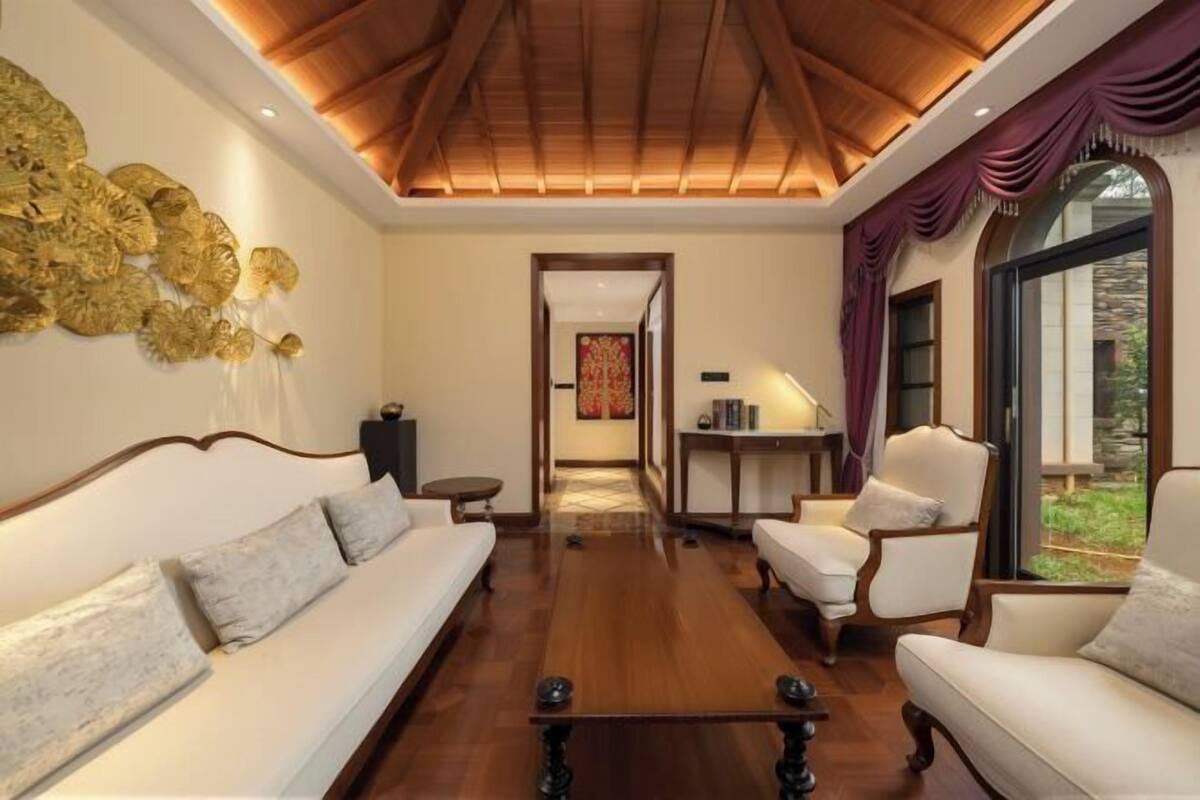 A spacious living room with a high ceiling, a sofa, armchairs, a coffee table, and a view through a glass door.