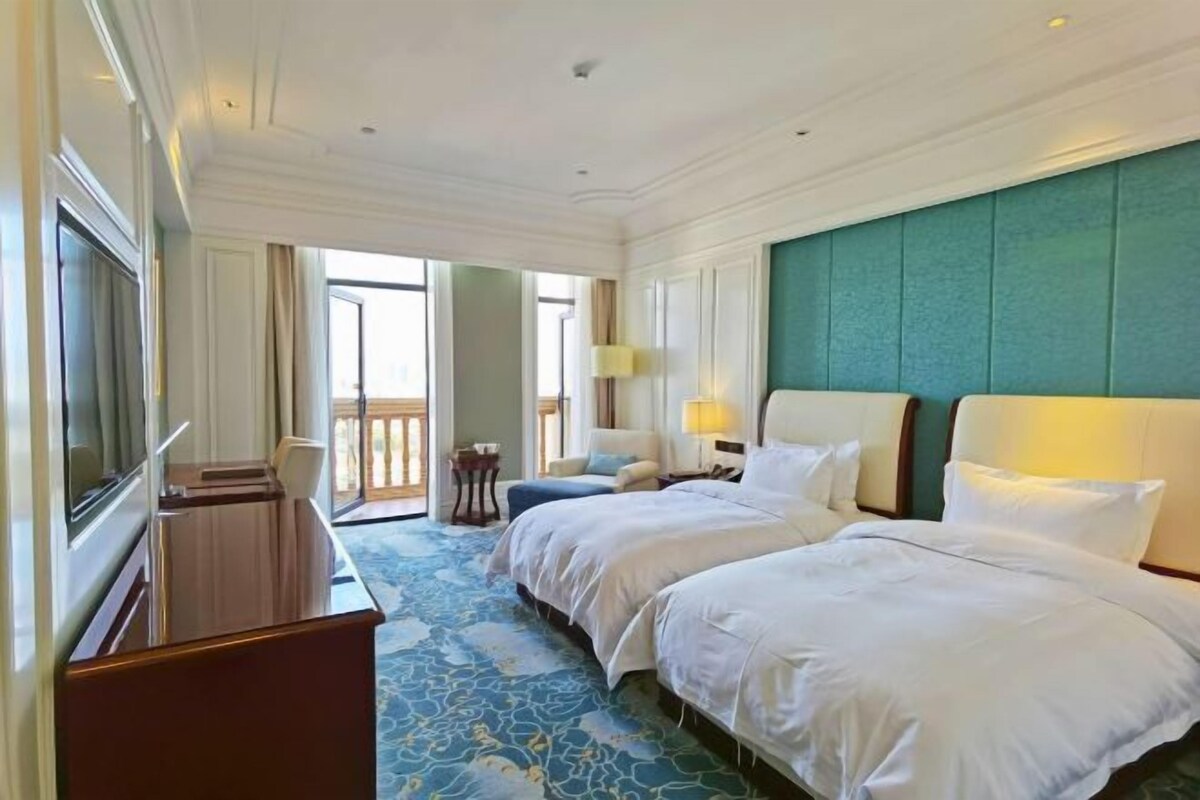 A hotel room with two beds, a TV, a desk, and a balcony.