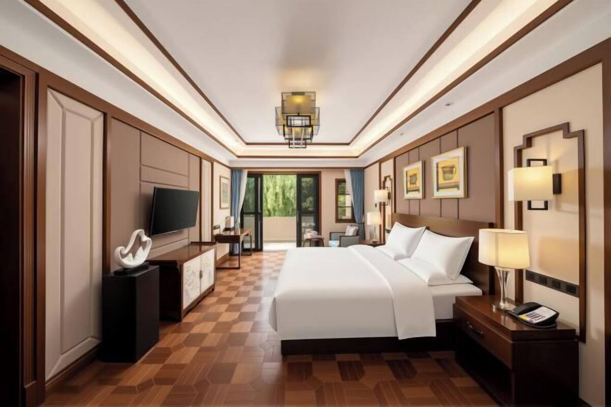 A hotel room with a large bed, a TV, a desk with a lamp, and a view of the outdoors.