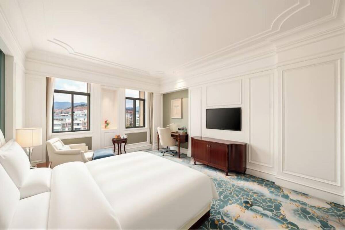 A hotel room with a large bed, a desk, a chair, a television, and a view of the city.