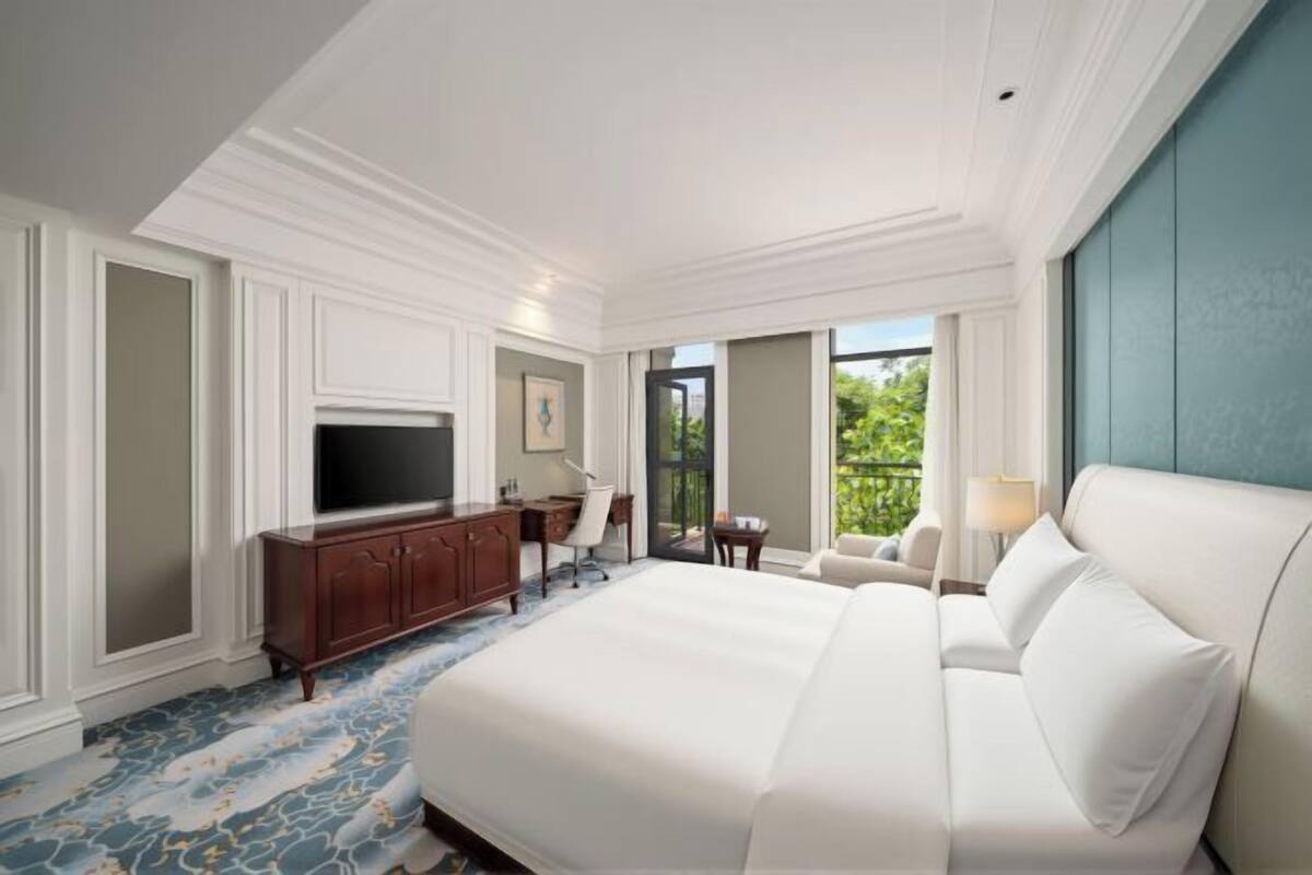 A large bed, a TV, a desk, and a chair in a hotel room with a view.