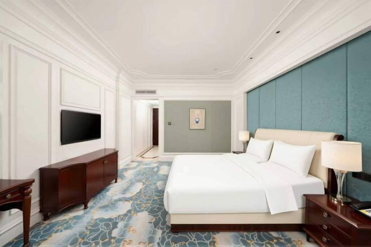 A hotel room with a large bed, a TV, a dresser, and a blue accent wall.