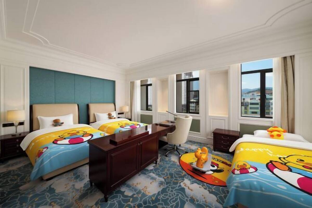 A hotel room with two beds, a desk, a chair, and a view of the city.