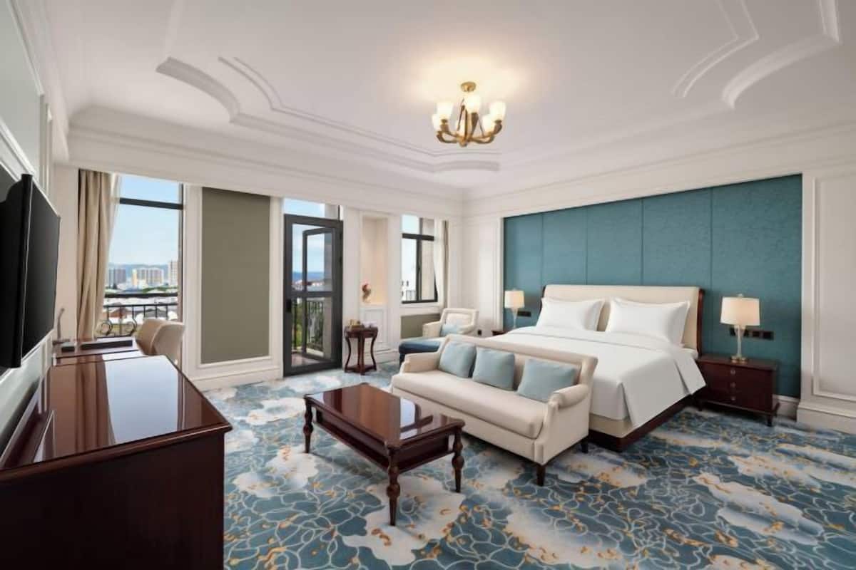 A hotel room with a bed, a desk, a sofa, a TV, and a view of the city.