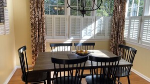 A dining room with a wooden table, black chairs, a chandelier, and a window with shutters.