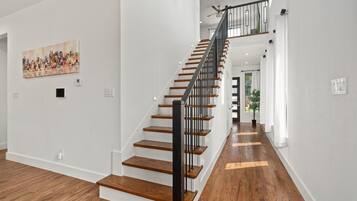 Un intérieur moderne avec un escalier en bois, des murs blancs et un tableau représentant un paysage urbain.