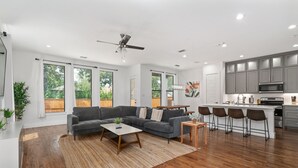 Ein geräumiger Wohnbereich mit grauem Sofa, Holztisch und einer Küche mit grauen Schränken und weißer Arbeitsplatte.