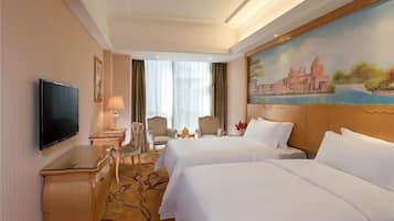 A hotel room with two beds, a TV, a desk, and a painting of a cityscape.