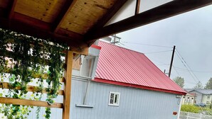 A wooden deck with metal chairs and a table, overlooking a house with a red roof.