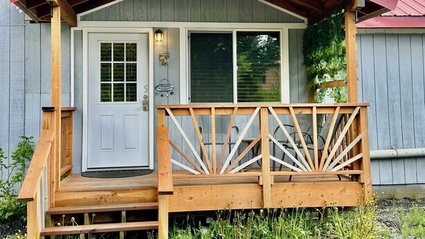A wooden cabin with a red roof, a front door, and a porch with wooden railings.