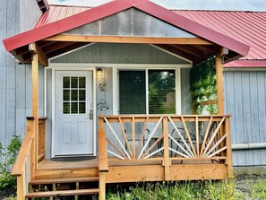 A wooden cabin with a red roof, a front door, and a porch with wooden railings. - Sweet one bedroom, 2 beds at the bakery (HAINES)
