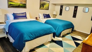 A hotel room with two beds, a desk, a lamp, and artwork on the walls.