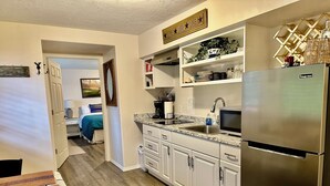 A modern kitchen with white cabinetry, a stainless steel refrigerator, and a built-in microwave. There is a coffee maker, a sink, and a small countertop with a plant and decorative items.