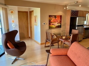 Un salon moderne avec un canapé incurvé, une table basse en verre et un coin repas avec des chaises. On y trouve également une cuisine équipée d’un réfrigérateur et d’une table à manger.