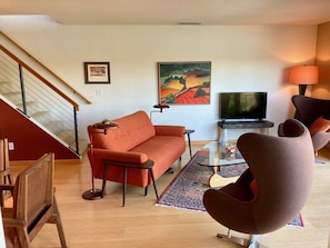 Un salon comprenant un canapé, des fauteuils, une table basse, un téléviseur et un escalier.