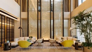 Un vestíbulo moderno con techo alto, ventanas amplias y una zona de estar con sillas amarillas y sofás blancos.
