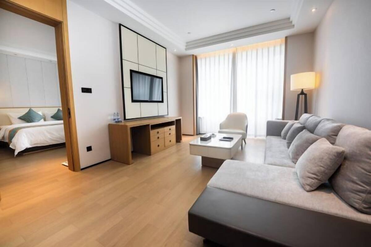A modern hotel room with a bed, a sofa, a TV, a desk, and a lamp.