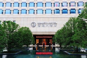 Un edificio de hotel con fachada moderna, un cartel que indica que es el Hotel Xiangyi y una piscina reflectante al frente.