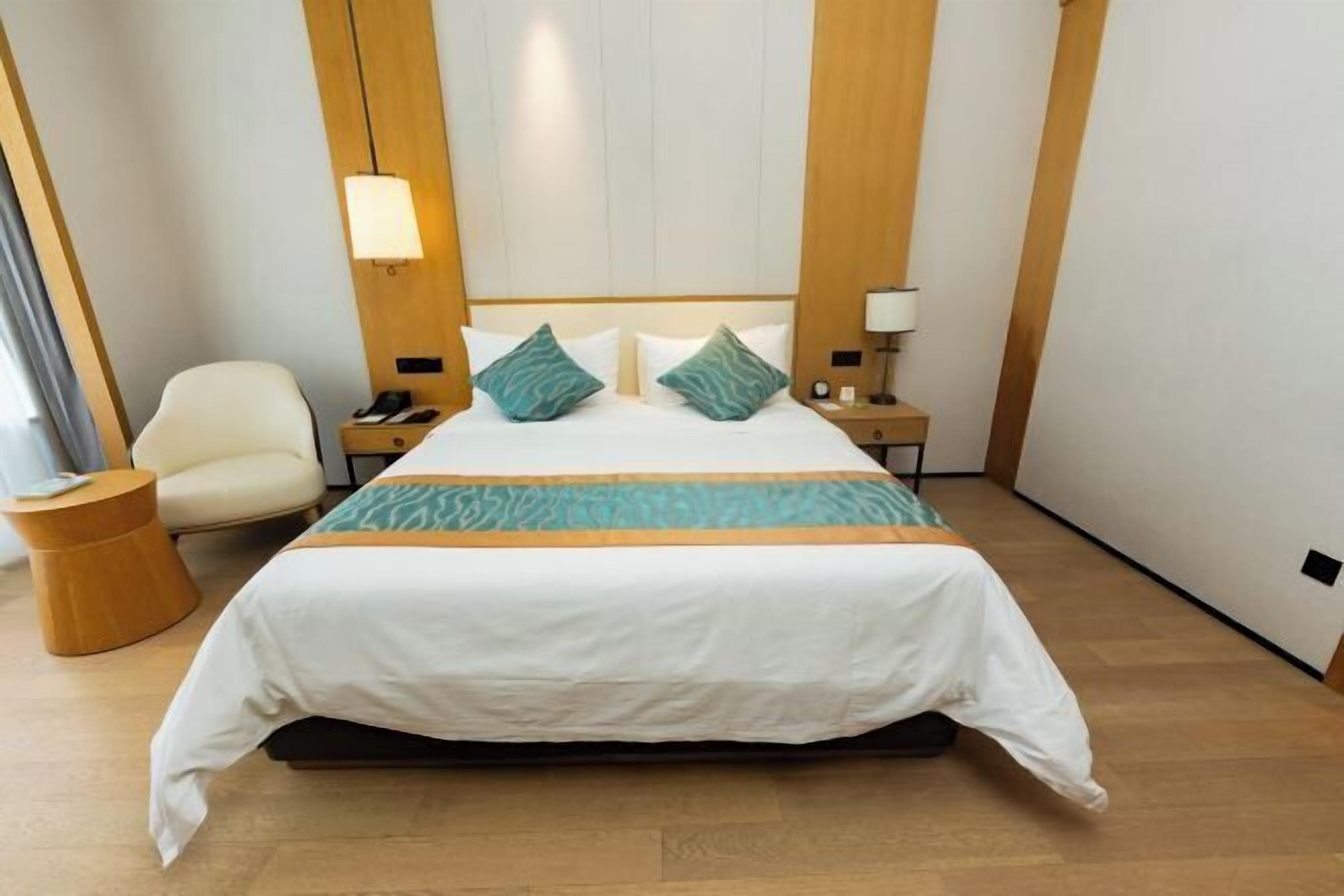 A hotel room with a bed, a chair, a bedside table, and a lamp.