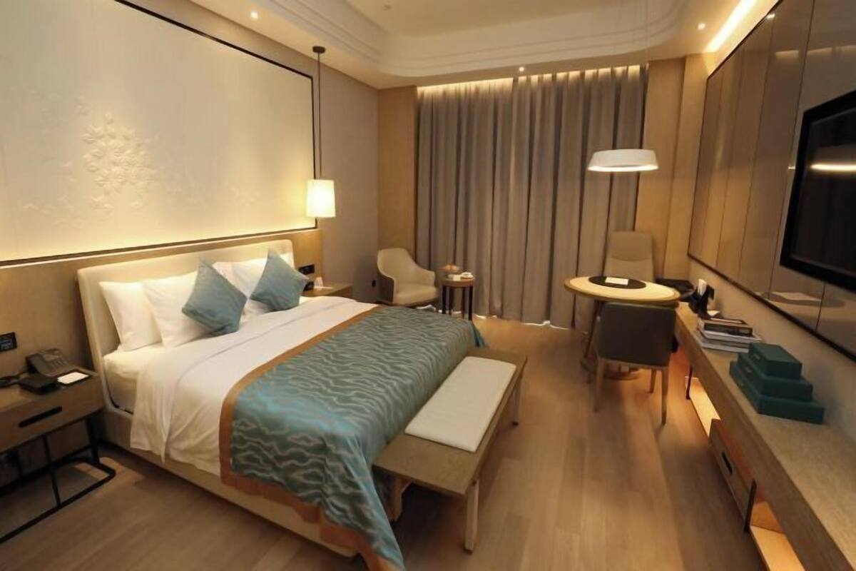 A modern hotel room with a bed, bedside table, lamp, chair, and a TV.