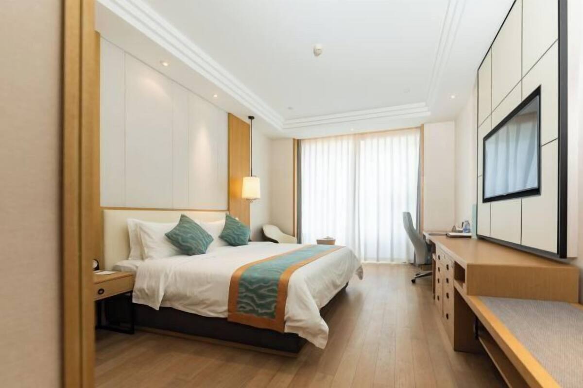 A hotel room with a bed, bedside table, desk, chair, and a TV mounted on the wall.