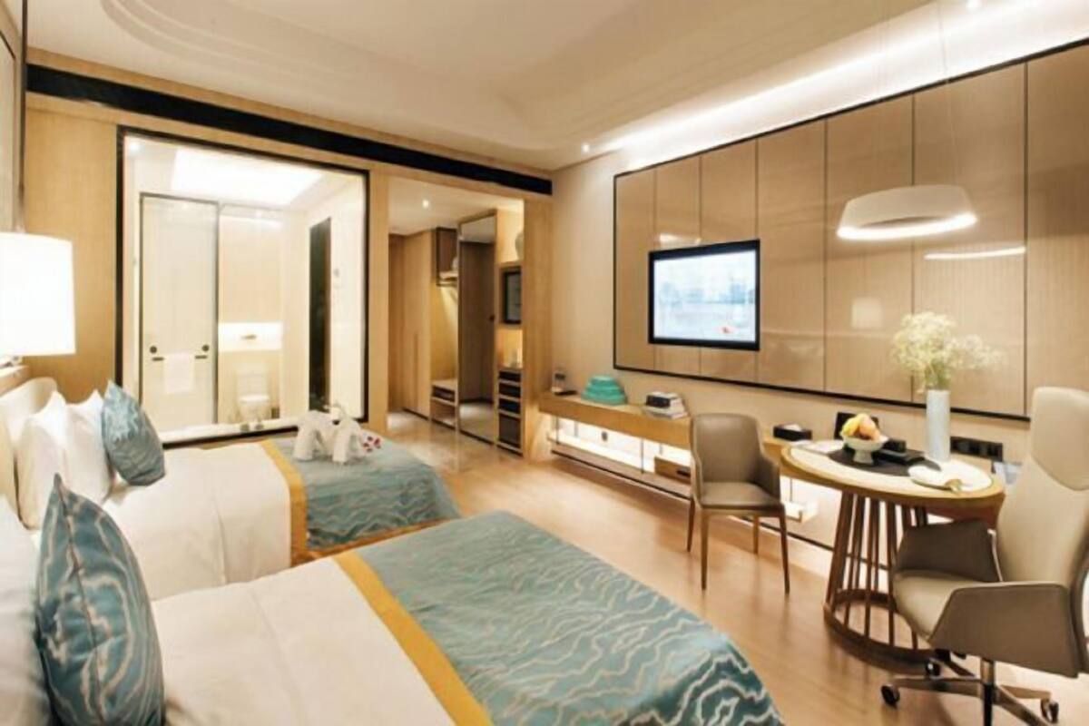 A hotel room with two beds, a desk, a chair, a television, and a large mirror.