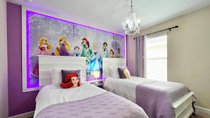 A bedroom with two beds, a chandelier, and a wall with Disney princess decorations.